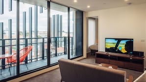 Un salon moderne doté d’un grand téléviseur, de sièges confortables et d’un balcon offrant une vue sur la ville.