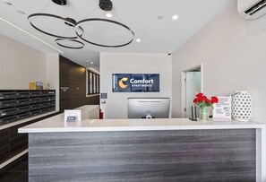 A reception desk with a 'Comfort Apartments' sign, a computer, and a visitor's box. - City Edge BOX Hill Apartment Hotel (Melbourne)