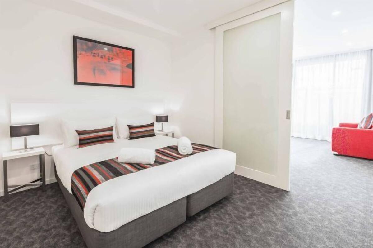 A hotel room with a large bed, two bedside tables with lamps, a red sofa, and a framed picture on the wall.
