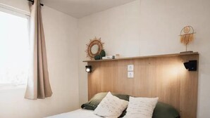 Una cama bien hecha con cabecera, lámpara de noche y un adorno en la pared.