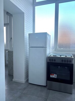 A kitchen with a white refrigerator, a stove, and a window with frosted glass. - Domus Lombardi Self Check-in Relaxation House with Jacuzzi (Roma)