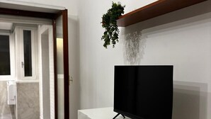 Ein modernes Wohnzimmer mit einem Flachbildfernseher auf einer weißen Konsole, einem Holzboden darüber und einer Topfpflanze.