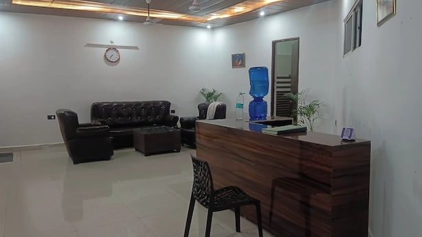 A reception area with a wooden reception desk, a black leather sofa, and a black chair. - Hotel Vidya Dham Vrindavan  (Mathura)