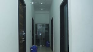 A corridor with a tiled floor, a glass door at the end, and a blue trash bin. - Hotel Vidya Dham Vrindavan  (Mathura)