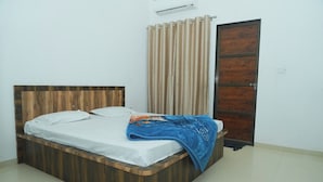 A bed with a wooden headboard, a white mattress, and a blue blanket. - Hotel Vidya Dham Vrindavan  (Mathura)