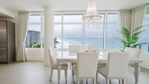 A dining area with a large table and chairs, a chandelier, and a view of the ocean. - Cobalt Horizon - Luxury beachfront 3 bedroom with panoramic gulf views (Destin)