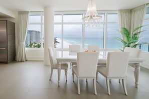 A dining area with a large table and chairs, a chandelier, and a view of the ocean. - Cobalt Horizon - Luxury beachfront 3 bedroom with panoramic gulf views (Destin)