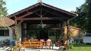 A covered outdoor seating area with benches and chairs, surrounded by potted plants and flowers. - ZEcamping 3* piscine pet friendly mobil-home BBQ 5 pers (Sandrans)