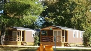 Deux maisons mobiles dotées de terrasses en bois, avec une structure de jeux pour enfants en premier plan.