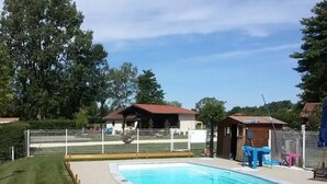Une piscine entourée d’une clôture, un petit bâtiment et une pelouse.
