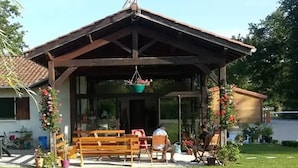 Un espace extérieur abrité, doté de bancs et de chaises, et agrémenté de plantes et de fleurs en pot.