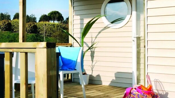 A wooden deck with a white chair and a table, a round mirror on the wall, and a bag on the deck. - ZEcamping 3* piscine dog friendly mobil-home BBQ 6 pers (Sandrans)