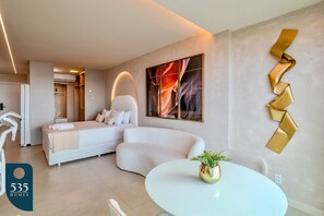 A modern hotel room with a curved bed, a round dining table, and a large abstract painting on the wall. - Wake up in Armação with a wide ocean view (Salvador)