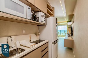 A modern kitchen with a stainless steel sink, a microwave, and a refrigerator. There is a countertop with a knife block and a small plant. - Wake up in Armação with a wide ocean view (Salvador)
