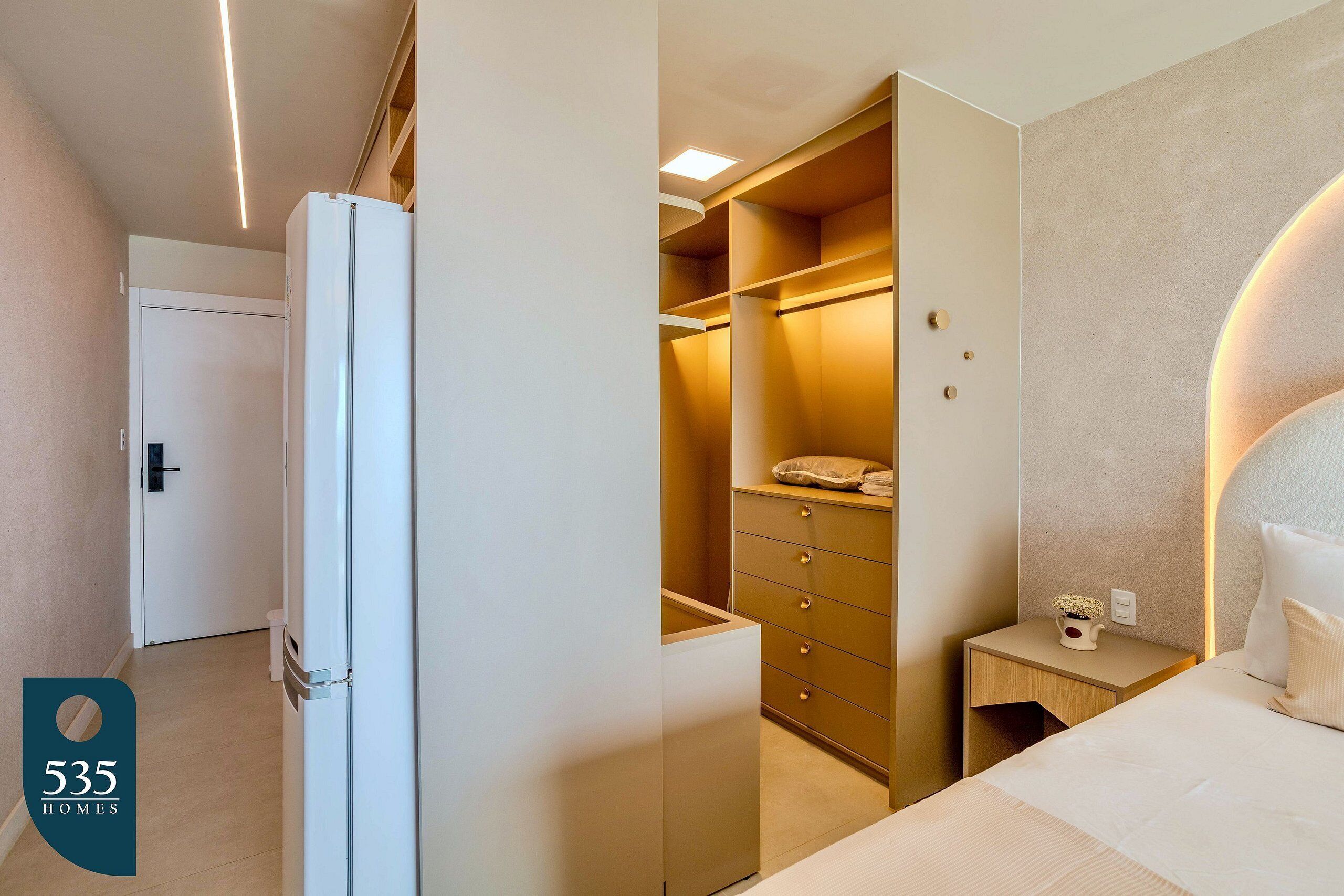 Et hotelværelse med seng, natbord, skuffer og hylder i et walk-in closet.