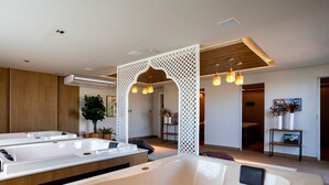 Ein moderner Wellnessraum mit zwei großen Badewannen, einer Holzvertäfelung, einer weißen Trennwand und einem kleinen Tisch mit Blumenvase und Bild.