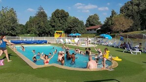 Uma piscina com pessoas aproveitando a água, cercada por grama e árvores.