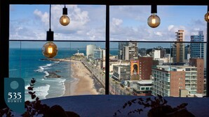 Blick von einem Hotelzimmer im Hochhaus auf Strand und Stadtlandschaft, mit hängenden Glühbirnen und einem Schild, das 535 Wohneinheiten anzeigt.