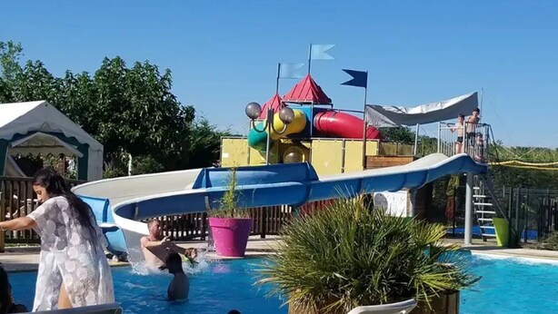 Una piscina con tobogán de agua, sillas de descanso y una carpa.