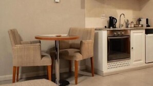 A compact kitchen with a dining table and chairs, a built-in oven, and white cabinetry. - Las Bayas Home Suites (Esquel)