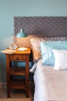 A neatly made bed with a patterned headboard, a bedside table with a lamp, and a clear glass bottle.