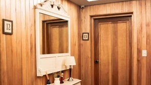 A room with wooden paneling, a vanity with a mirror, a lamp, and a bottle of wine. There are two doors, one with a number 12 and the other with a number 13. - Las Bayas Home Suites (Esquel)