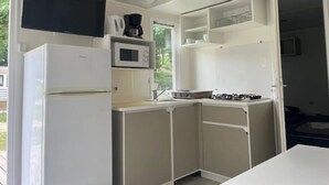 A compact kitchen with a refrigerator, microwave, stove, and a flat-screen TV mounted above the counter. - Camping 3 étoiles - Piscine  - ccbfa0c (Saint-Mandé-sur-Brédoire)