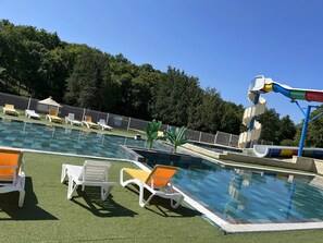 A swimming pool with multiple lanes, surrounded by white lounge chairs and a water slide. - Camping 3 étoiles - Piscine  - ccbfa0h (Saint-Mandé-sur-Brédoire)