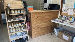 Una encimera de madera con tarros de miel y panales, un extintor y un tablón de anuncios con varios avisos.