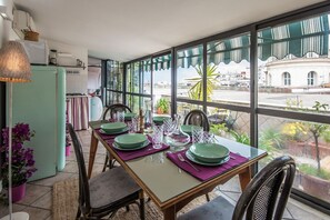 Un coin repas avec une table dressée pour quatre personnes, de grandes fenêtres offrant une vue sur la ville et, au fond, une petite cuisine.