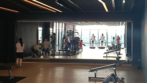 A gym with wooden flooring, exercise equipment, and a large mirror reflecting the space.