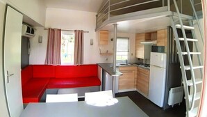 Eine kompakte Küche mit Essbereich, einem roten Sofa und einem Schlafzimmer auf dem Dachboden, erreichbar über eine Leiter.