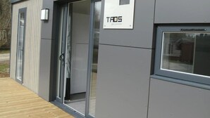 Um edifício moderno com fachada cinzenta, porta com painel de vidro e uma placa com a inscrição "TAOS par Louisiane".