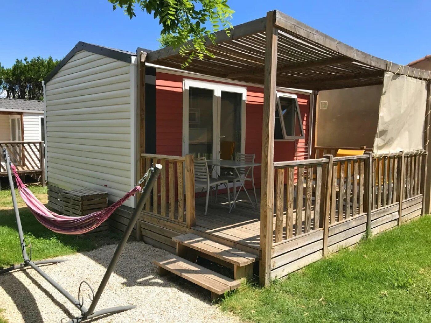 A small, single-story mobile home with a wooden deck and a covered patio area.