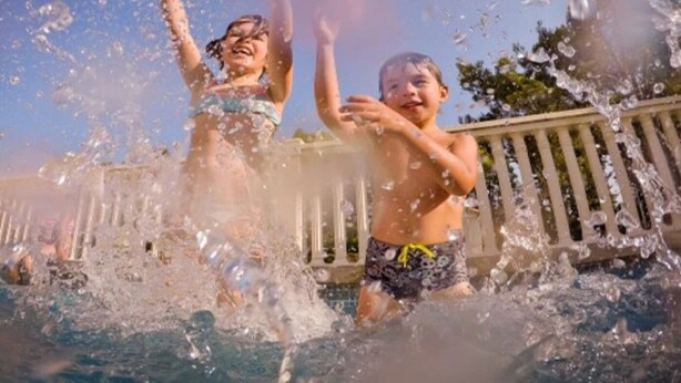 Twee kinderen spelen in een zwembad, water spat eromheen.