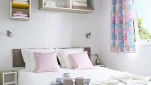 Een keurig opgemaakt slaapkamer met een bed, nachtkastjes en een plank met opgevouwen handdoeken.
