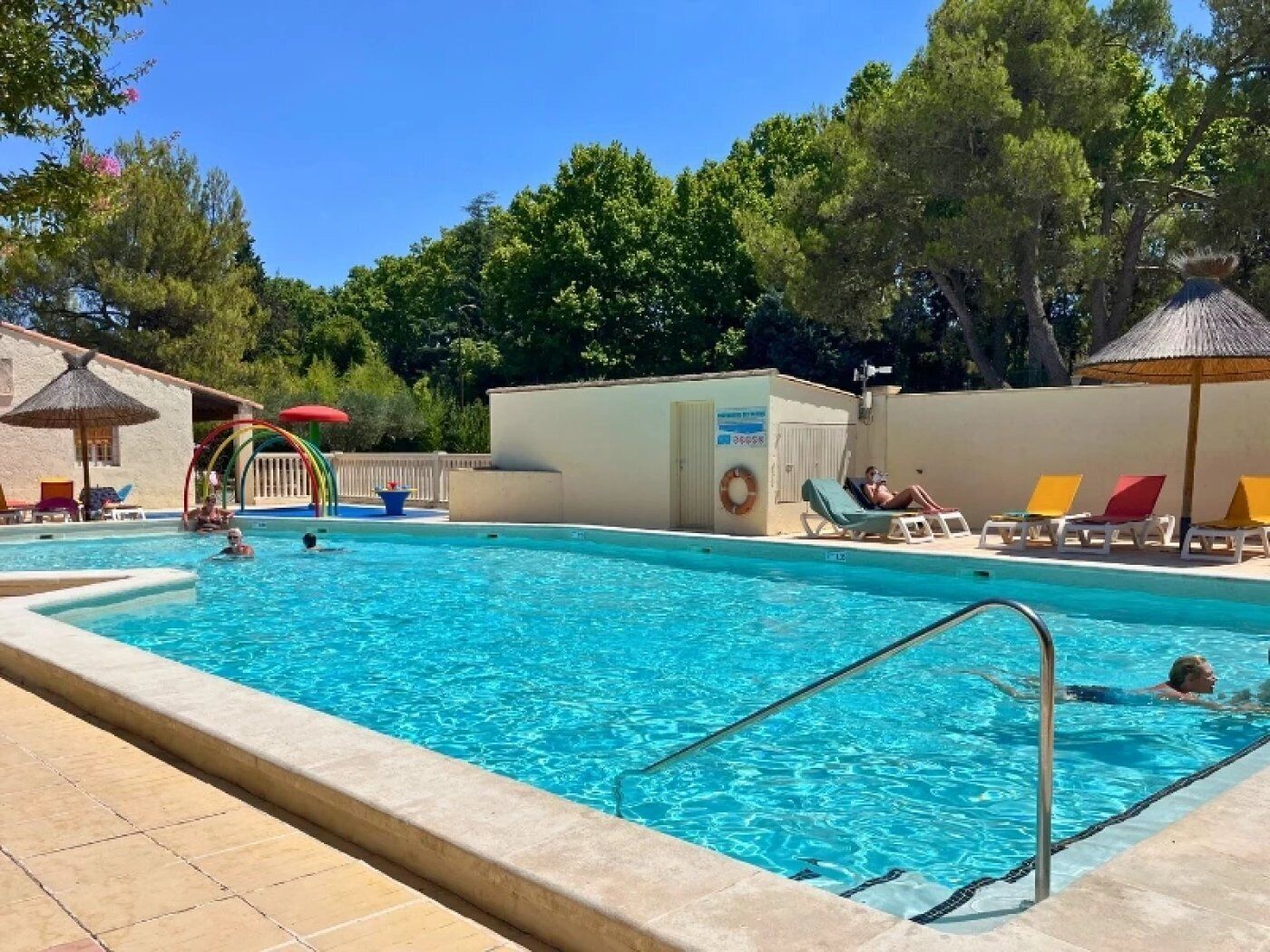 A swimming pool with lounge chairs and umbrellas, surrounded by trees.