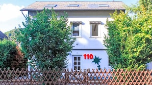 Un edificio blanco con el número 110 en la fachada, rodeado de árboles y una valla de madera.