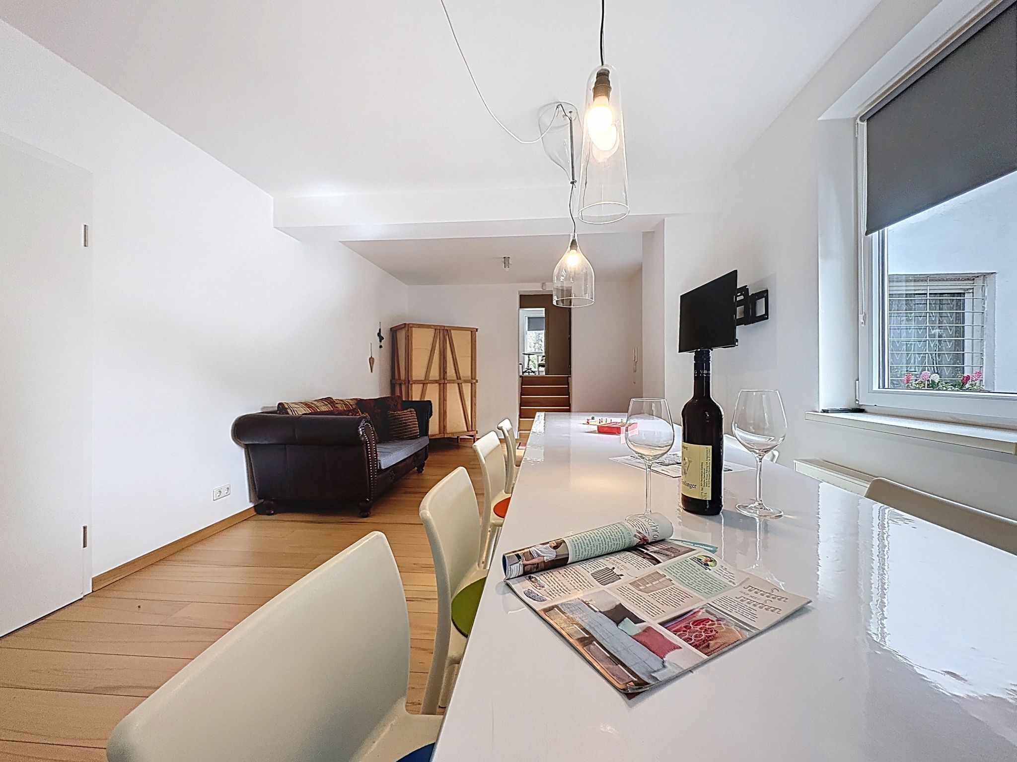 Un salon moderne comprenant un coin repas, un canapé, une table avec un magazine et une bouteille de vin.