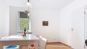 Un coin repas comprenant une table, des chaises, une bouteille de vin et une fenêtre donnant sur des arbres.