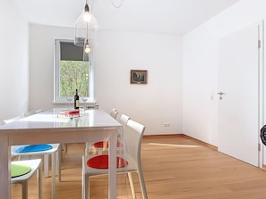 A dining area with a table, chairs, a bottle of wine, and a window with a view of trees.