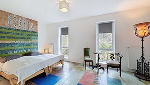 Une chambre à coucher avec un lit, une chaise, une table, un mur orné de chiffres et un sol à motifs colorés.