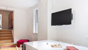 Une pièce avec une table blanche, une chaise rouge, un jeu d’échecs et un téléviseur fixé au mur.
