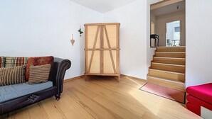 Une pièce dotée d’un plancher en bois, d’un canapé agrémenté de coussins à motifs, d’une armoire en bois et d’un escalier menant à un autre espace.