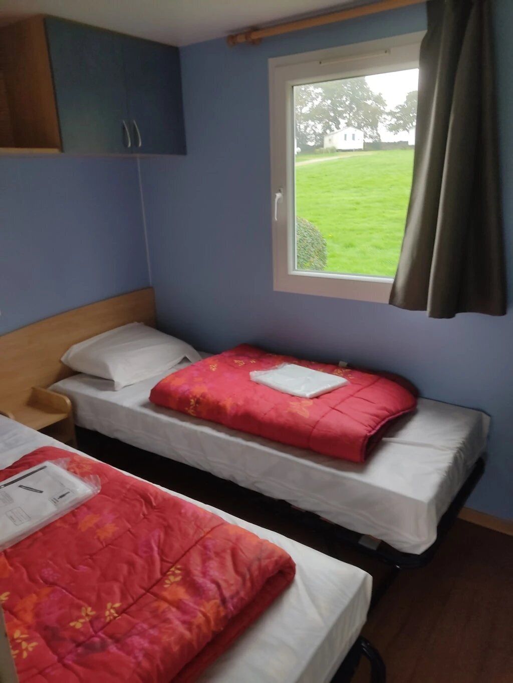 Een kamer met twee bedden, een raam met uitzicht op een gazon en een houten hoofdeinde.