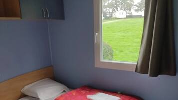 Een kamer met twee bedden, een raam met uitzicht op een gazon en een houten hoofdeinde.
