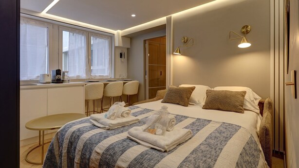 Ein modernes Hotelzimmer mit Bett, Nachttischen, einem Schreibtisch und einem Sessel.