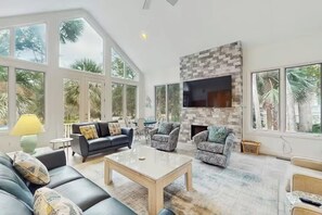 A spacious living room with a fireplace, large windows, and comfortable seating. - Lagoon Path to Beach | Pool & Golf (Hilton Head Island)