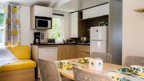 Eine kompakte Küche mit Mikrowelle, Toaster und Kühlschrank. Ein Esstisch mit Stühlen sowie eine Couch mit floralem Kissen sind vorhanden.