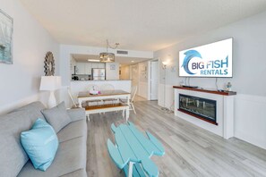 A modern living room with a sofa, a dining table, and a TV displaying 'Big Fish Rentals' logo. - NEW Baywatch Remodeled with Direct Oceanfront View (North Myrtle Beach)
